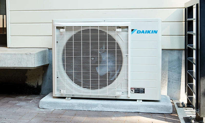 Daikin FIT installed beside a home and outdoor patio, manufacturer installation example