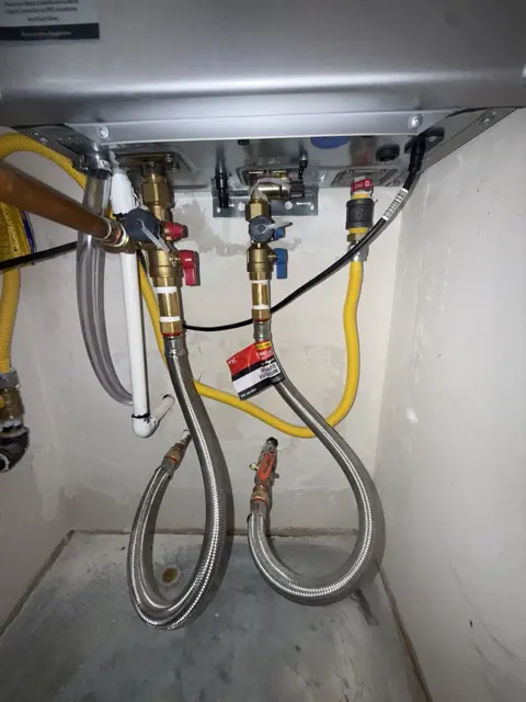 Water and gas piping beneath a wall-mounted tankless water heater.