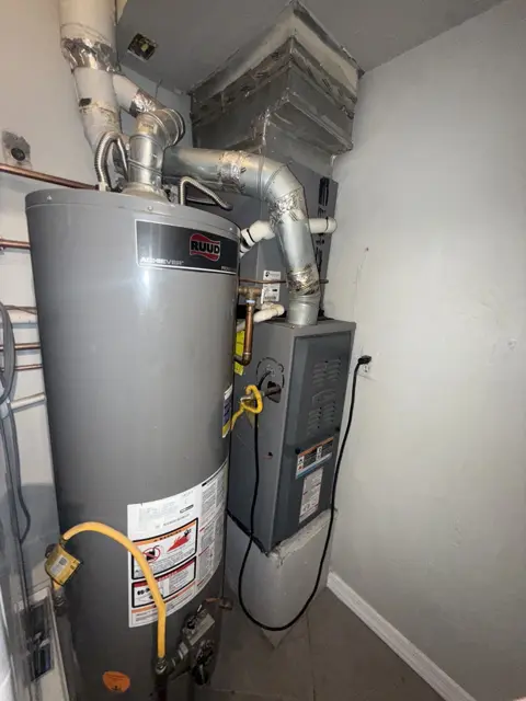 A tank water heater beside a furnace, with overhead vent connections.