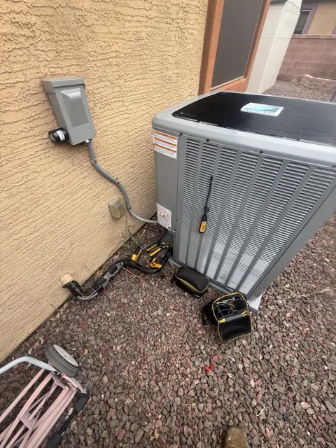 Outdoor HVAC equipment beside a stucco wall, with service connections visible.
