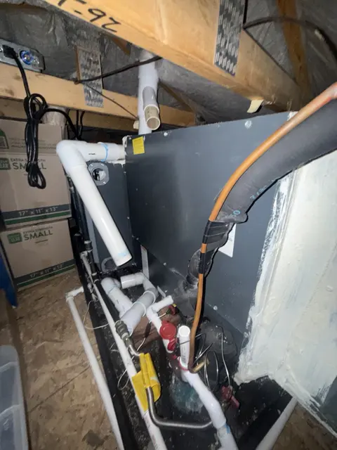 Indoor HVAC equipment with refrigerant lines and condensate piping in an attic.